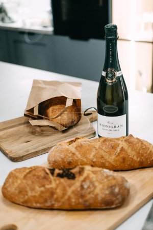 Téléchargez les photos : Une bouteille de Franciacorta Brut élégamment affichée avec du pain artisanal fraîchement cuit sur un comptoir de cuisine. - en image libre de droit