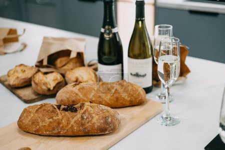 Photo for Food and Beverage Pairing. Freshly baked artisan bread paired with sparkling and white wine on a modern kitchen countertop. - Royalty Free Image
