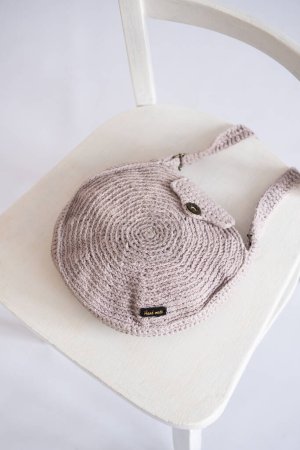 crafted handmade crocheted shoulder bag in a soft pink hue, displayed on a white chair, symbolizing artisanal fashion and creativity.