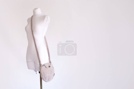 A neutral-toned handmade crocheted crossbody bag draped elegantly over a white mannequin, epitomizing artisanal fashion.