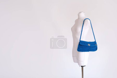 Eine lebendige blaue gehäkelte Schleudertasche auf einer weißen Schaufensterpuppe, die nachhaltige und ethische Modetrends verkörpert.