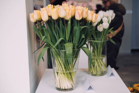 Superbes tulipes blanches et jaunes douces gracieusement disposées dans des vases en verre transparent, présentées lors d'une exposition sur les tulipes.