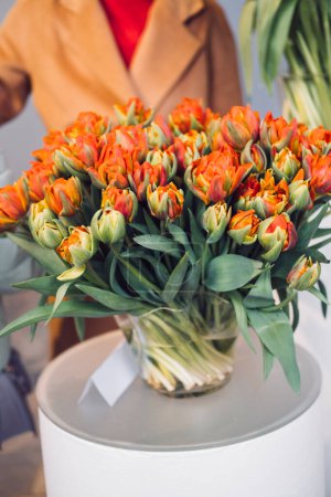 An exquisite display of parrot tulips, bursting with orange and red hues, presented in a glass vase during a varietal tulip exhibition.