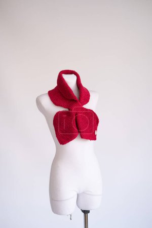 Vibrant red knitted scarf with unbranded text Handmade on the tag elegantly wrapped around a mannequin, highlighting a warm, sustainable knitwear accessory.