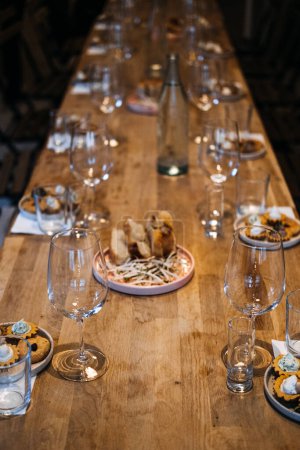 An inside look at the meticulous preparation for a professional wine tasting event, with artfully arranged glasses and culinary pairings on a wooden table.