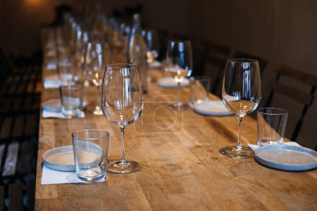 Una larga mesa de madera en una bodega con elegantes copas de vino, lista para una experiencia profesional de cata de vinos.