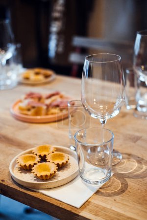 Gros plan de délicieuses tartelettes et canapés sur des assiettes à côté de verres à vin vides, posés sur une table en bois pour un événement sophistiqué de jumelage mets-vins.