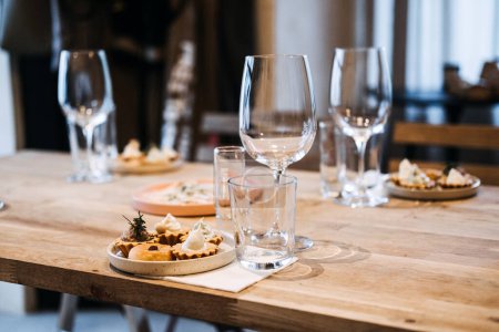 The serene setting of a wine culture event captured through the sophisticated arrangement of stemware and gourmet bites on a wooden table.