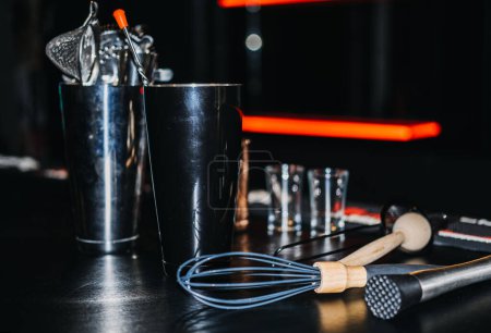 An array of professional mixology tools laid out on a bar, including shakers, strainers, and a whisk, ready for cocktail creation.