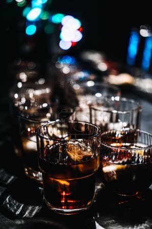 Dynamic scene of a bartender in action, pouring whiskey into several glasses, each filled with ice, set against the vibrant backdrop of a bustling bar.