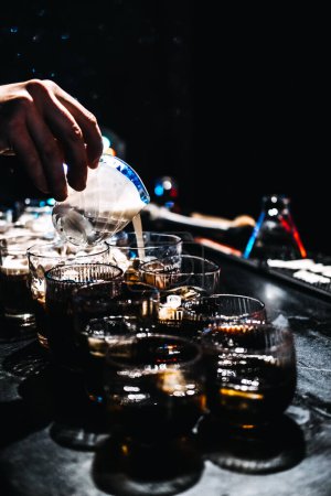 Photo for A bartender skillfully pours cream into coffee cocktails, creating a decadent blend in a dark, ambient bar setting, perfect for an evening treat. - Royalty Free Image