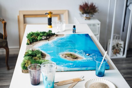 Intricately crafted 3D epoxy resin art featuring a stunning coastal landscape, displayed on a studio table, showcasing the artists skill and creativity.