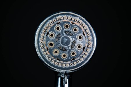 Hard water calcium or lime scale deposits on old, worn out shower head. Close up studio shot, isolated on black, no people.