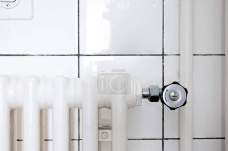 Photo for Cast iron home radiator thermostatic control valve. Front view, white ceramic bathroom tile wall, no people. - Royalty Free Image