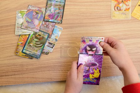 Photo for Arahal. Seville. Spain. 1st March 2023. Detail of a child's hands placing rare collectible Pokemon trading cards on a wooden table. Collectible trading cards based on the Pokemon anime series. - Royalty Free Image