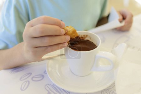 Detail of a child's hand dipping a churro in hot chocolate. Churros with chocolate are a typical breakfast in Spain.
