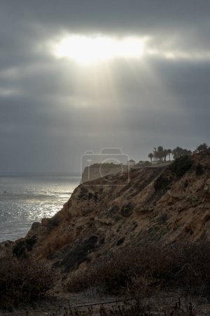 The rugged cliffs of Point Vicente are adorned with beams of light piercing through the overcast sky, highlighting the serene beauty of Rancho Palos Verdes and its scenic coastal trail.