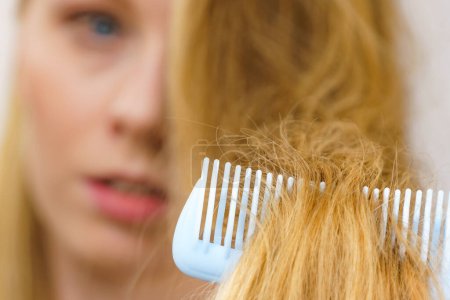 Blonde woman with comb brushing her very long messy hair. Teenage girl with bad hair care.