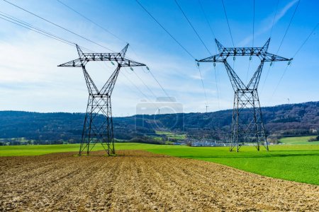 Electricity transmission pylons, power linee voltage towers in spring agricultural landscape.