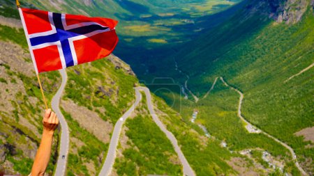 Norwegian flag and Trolls Path Trollstigen winding scenic mountain road in Norway Europe (en inglés). Ruta turística nacional.