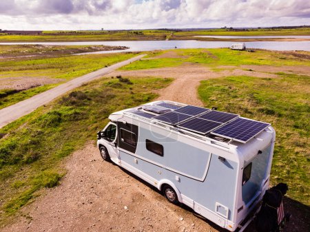 Aerial view of camper with many solar photovoltaic panels on roof camping on lake shore in Portugal. Renewable free energy. Caravan holidays.