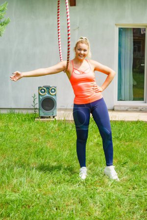 Woman using hoola hoop for slim fit body, doing exercises gym outdoor in garden. Workout training on fresh air. Active healthy lifestyle.