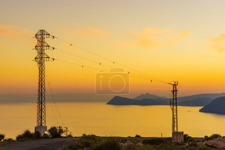 Coastline at sunset with electricity transmission pylons, power lines high voltage towers. Mesa Roldan, Cabo de Gata, Spain.
