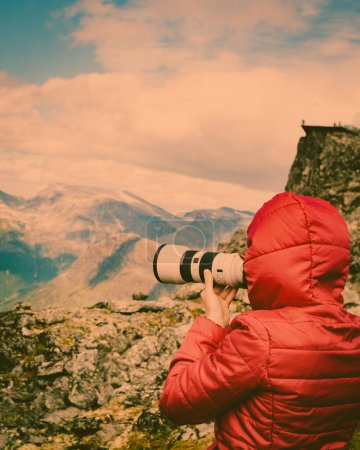 Female tourist taking photo with camera, enjoying mountains landscape from Dalsnibba area in Norway.