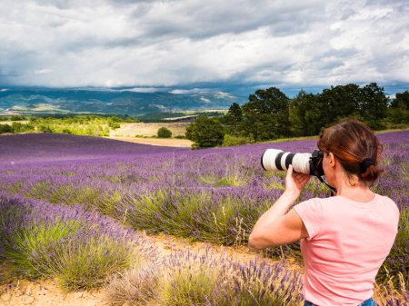 Mature tourist woman with camera taking travel photo from Provence landscape with purple lavender fields. Puimoisson region, Plateau Valensole, Alpes de Haute Provence in France