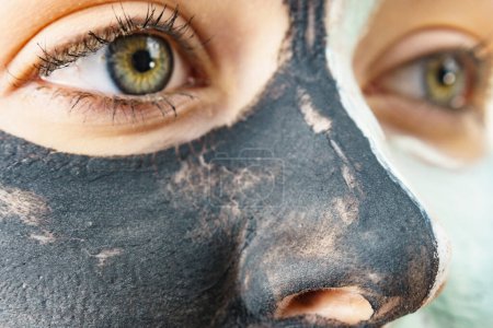Woman cleaning skin face, using green mud and carbo black mask. Girl taking care of oily complexion. Beauty and kincare.
