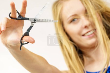 Young woman holding special chunking shears, tool for work of hairdresser. Coiffure hairstyle and haircut.