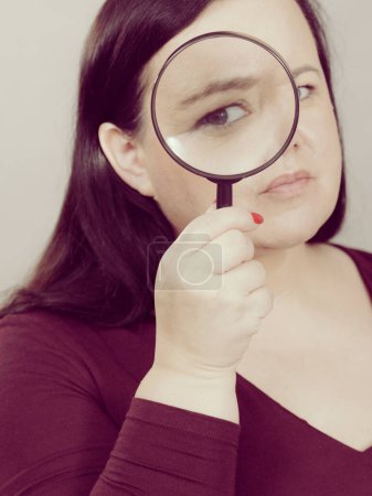 Adult woman holding magnifying glass investigating something and looking closely, trying to find solution.