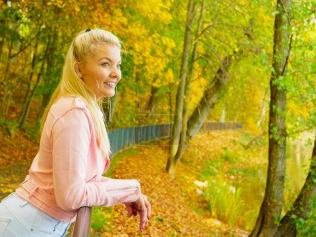 Blonde junge Frau im modischen Outfit. Glückliches Weibchen in pinkfarbener Lederjacke spaziert entspannt im Herbstpark.