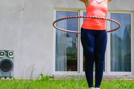 Woman using hoola hoop for slim waist, doing exercises gym outdoor in garden. Workout sport and training.