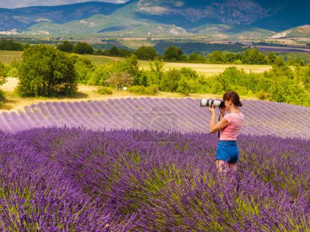 Mature tourist woman with camera taking travel photo from Provence landscape with purple lavender fields. Puimoisson region, Plateau Valensole, Alpes de Haute Provence in France