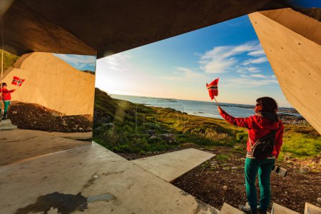 Touristin mit norwegischer Flagge genießt Meerblick vom Rastplatz Bukkekjerka auf der Insel Andoya, Vesteralen Archipel, Norwegen.