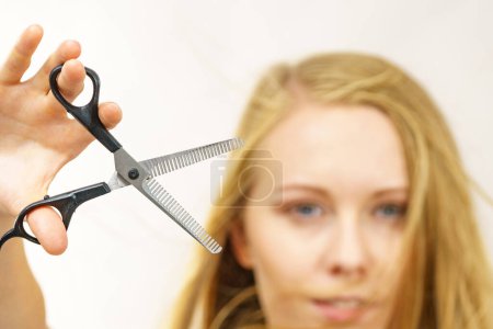 Young woman holding special chunking shears, tool for work of hairdresser. Coiffure hairstyle and haircut.