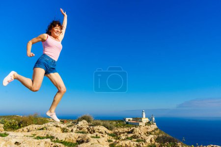 Woman enjoying trip with rv motor home, jumping in the air at camper. Mesa Roldan lighthouse location, Almeria Spain. Happiness and traveling.
