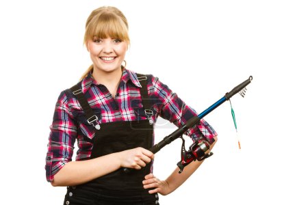 Fishing concept. Attractive woman in dungarees, pink check shirt holding rod. Isolated background