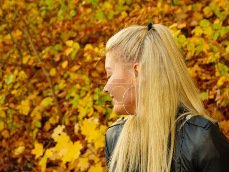 Blonde Frau im modischen Outfit. Glückliches Weibchen in schwarzer Lederjacke spaziert im herbstlichen Park und genießt den sonnigen Tag
