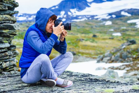 Turista mujer en las montañas en la alta pila de piedra tomando fotos de viaje con cámara. Ruta turística nacional 55 Sognefjellet, mirador de Mefjellet, Noruega