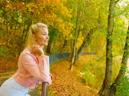 Blonde junge Frau im modischen Outfit. Glückliches Weibchen in pinkfarbener Lederjacke spaziert entspannt im Herbstpark.