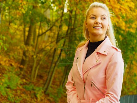 Mujer joven rubia con ropa de moda. Mujer feliz en piel rosa ramones chaqueta caminando relajante en el parque de otoño.
