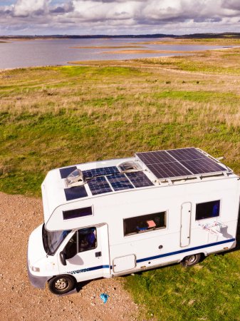 Aerial view of camper with many solar photovoltaic panels on roof camping on lake shore in Portugal. Renewable free energy. Caravan holidays.