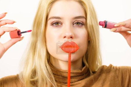 Young adult woman applying lipstick or lip gloss, getting her make up done holding fake lips on stick