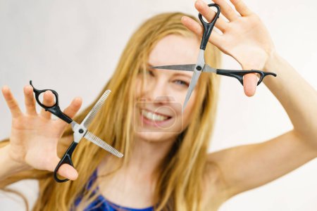 Chica con el pelo rubio soplado largo sosteniendo tijeras, mostrando herramientas de trabajo, tijeras normales y cortantes. Haciendo peinado, peinado nuevo. Concepto de cuidado del cabello.