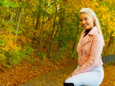 Mujer joven rubia con ropa de moda. Mujer feliz en piel rosa ramones chaqueta caminando relajante en el parque de otoño.
