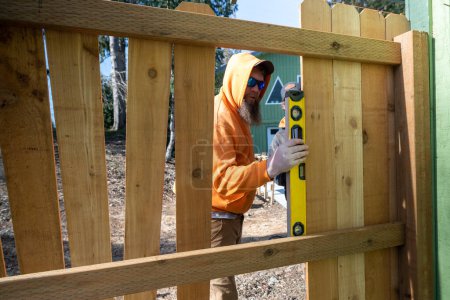 Photo for Using a Level Tool to Measure Wood Pickets on Fence For Leveling on Work in Progress - Royalty Free Image