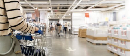 Photo for Soft focus woman with shopping cart at store, for furniture in warehouse. Many big metal shopping carts for the interior furniture on a parking lot for the customer use shopping in the warehouse store. - Royalty Free Image
