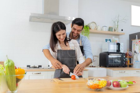 Photo for Young couple having fun while preparing breakfast together in a beautiful morning, cooking together, kitchen relationship, slicing tomatoes together.Love of a couple. Vegetable salad for breakfast - Royalty Free Image